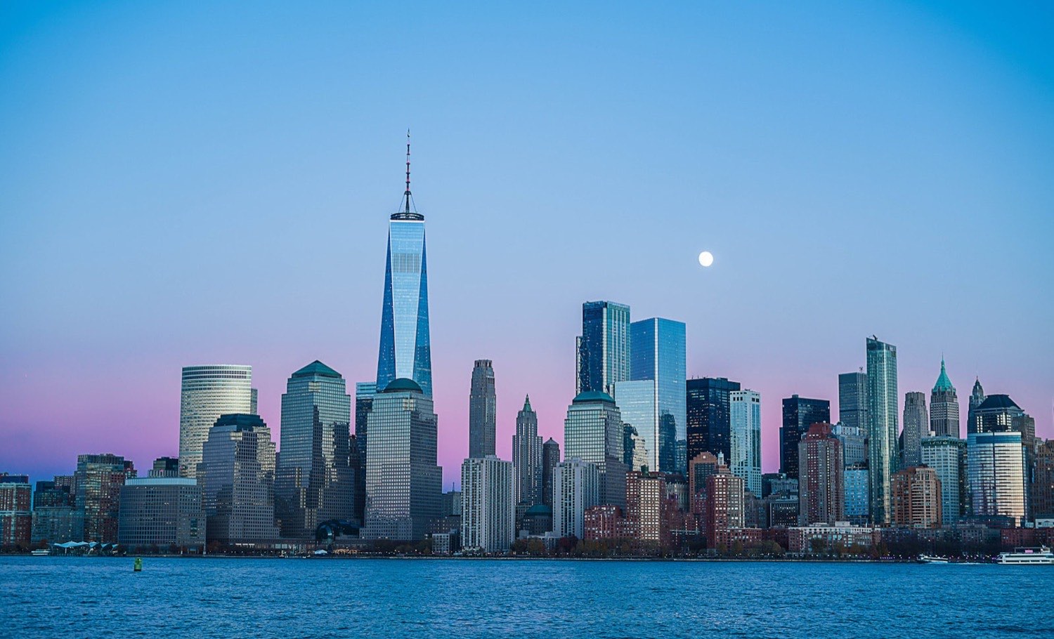 The Lower Manhattan skyline at dusk, seen across New York Harbor